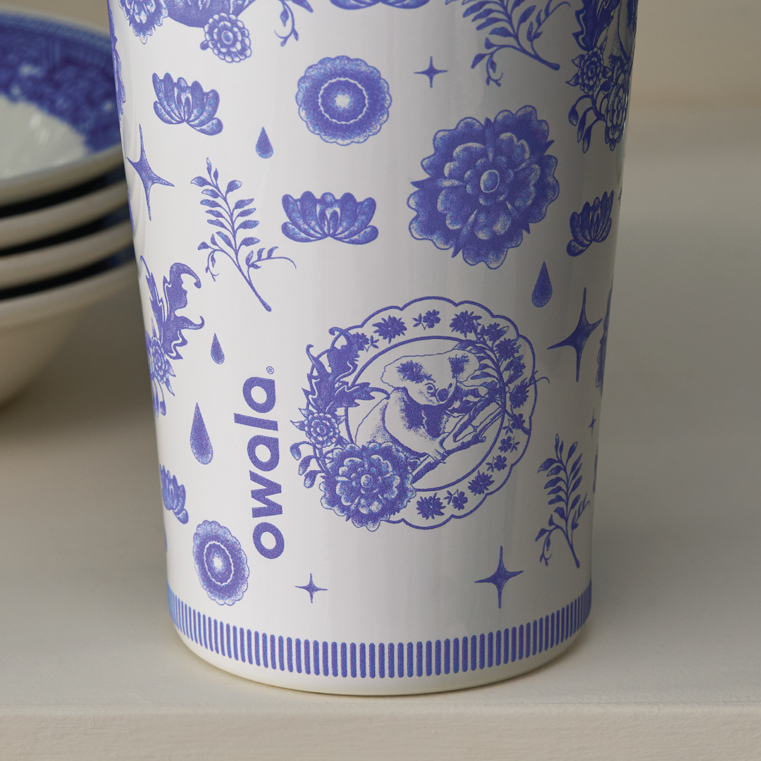 Lower body of an Owala bottle showing the cobalt blue floral medallion print over white with the Owala logo, displayed next to white bowls